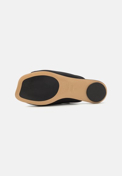 Svart såle med en beige mellomsåle, rund form, flat overflate og teksturert svart gummibunn. Merkingene inkluderer merke og størrelsesdetaljer.