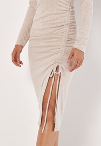 Abito lungo beige chiaro con texture arricciata, maniche lunghe e spacco laterale legato con fasce coordinate. Tessuto morbido con un motivo sottile.