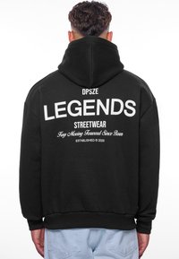 Sort hætte sweatshirt med stort hvidt tekst, der står "LEGENDS", samt yderligere trykte detaljer på ryggen. Blødt stof, afslappet pasform.