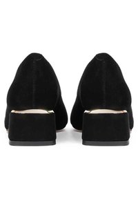 Chaussures à talons noires en daim avec un bout pointu et un talon bloc court et solide. La texture semble douce, avec une doublure intérieure lisse.