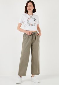 Witte cropped t-shirt met bloemenontwerp; losse olijfgroene broek met elastische tailleband; gedragen met witte sneakers.