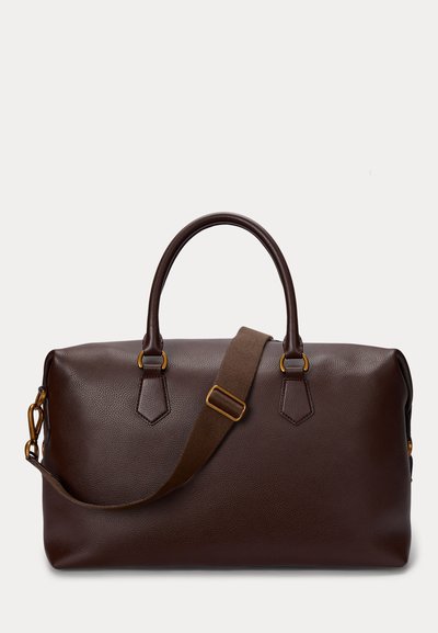 Tumši brūna ādas duffel soma ar divām rokturiem un regulējamu plecu siksnu ar misiņa detaļām uz balta fona.