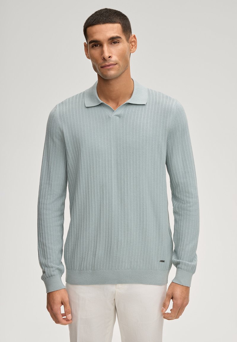 Hellblaues langärmliges Poloshirt aus strukturiertem Stoff, mit V-Ausschnitt und weichem Kragen. Legere Passform mit gerippten Bündchen.