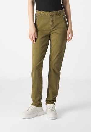 Pantaloni verde oliva con vestibilità slim, realizzati in tessuto morbido, dotati di tasche con zip e una texture liscia. Abbinati a sneakers bianche.