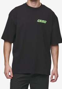 Czarna bawełniana koszulka z luźnym krojem. Posiada małe zielone logo graficzne na lewej piersi, krótkie rękawy oraz okrągły dekolt.