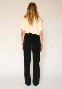 Pantalons en velours côtelé noirs à taille haute et jambes larges, associés à un haut court de couleur claire. La texture est douce et nervurée.