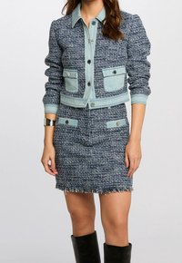 Granatowa teksturowana kurtka z jasnoniebieskimi akcentami z denimu, wyposażona w dwie przednie kieszenie i dopasowaną spódnicę z wystrzępionym dołem. Czarne kozaki za kolano.