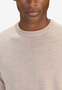 Beige stickad tröja med rund hals. Har en slät textur och klassisk passform, som framhäver en enkel design och minimal detaljer.