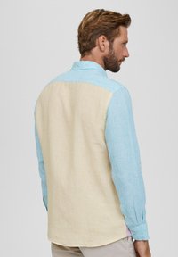 Mehrfarbiges Langarmhemd mit vertikalen Streifen in Blau, Gelb und Hellblau. Klassischer Kragen und abgerundeter Saum. Strukturierter Stoff.