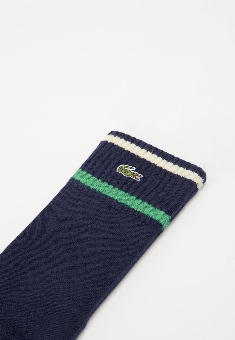 Granatowa skarpetka z zielonymi i białymi paskami w górnej części oraz małym, haftowanym zielonym logo krokodyla na prążkowanym mankiecie.
