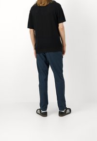 Černý pruhovaný top s krátkým rukávem, modré kalhoty a černé tenisky s bílými pruhy, z pohledu zezadu na bílém pozadí.