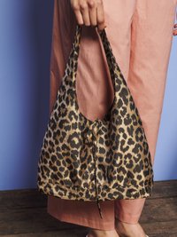 Rankomis laikoma leopardų rašto audinio pirkinių maišas su užrištu raiščiu, apsivilkus laisvas rožines kelnes, stovint mediniais grindimis.