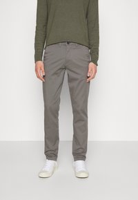Gray cotton pants with a straight leg design, paired with a green long-sleeve shirt. Models white sneakers. Minimalistic aesthetic.