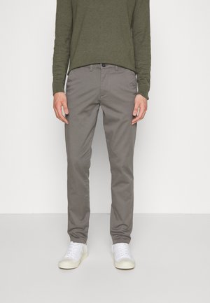 Pantaloni di cotone grigi con un design a gamba dritta, abbinati a una camicia verde a maniche lunghe. Modelli scarpe da ginnastica bianche. Estetica minimalista.