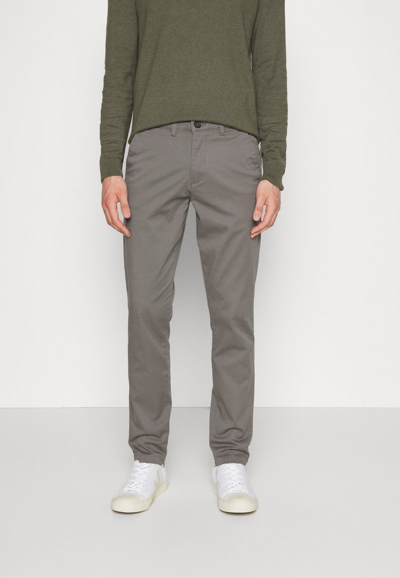 Gray cotton pants with a straight leg design, paired with a green long-sleeve shirt. Models white sneakers. Minimalistic aesthetic.