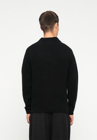 Schwarzer gestrickter Pullover mit Kragen, locker sitzend und mit gerippten Bündchen. Weicher Textil, schlichtes Design und keine sichtbaren Verzierungen.