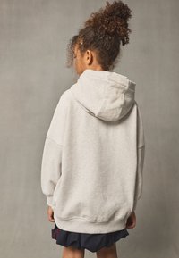 Grauer übergroßer Hoodie mit Kängurutasche und Tunnelzugkapuze. Weicher, strukturierter Stoff mit lockerem Schnitt.