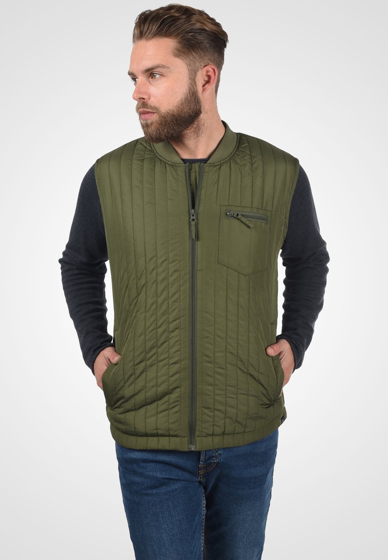 Quilted maslinasto zeleni prsluk s visokim ovratnikom, zatvaranjem na zip i džepom na prsima; opremljen tamnim rukavima i bočnim džepovima. Izdržljiv materijal.