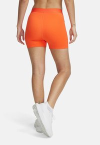 Helderoranje sportshorts met een aansluitend ontwerp, een gladde textuur en een brede elastische tailleband, gedragen met witte sportschoenen.