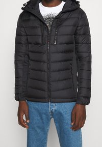 Giacca a vento nera con chiusura a zip, cappuccio e due tasche frontali con zip. Presenta pannelli cuciti e polsini elastici per una vestibilità ottimale.