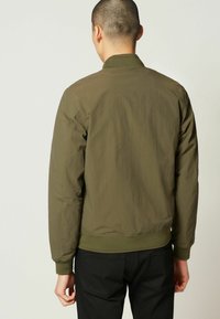 Olivgrüne Bomberjacke mit strukturiertem Finish, geripptem Kragen und Bündchen sowie einem taillierten Saum. Keine sichtbaren Logos oder Verzierungen.