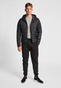 Sort dunjakke med hætte, med quiltet design. Sammen med grå t-shirt og sorte joggingbukser. Inkluderer sorte sneakers.