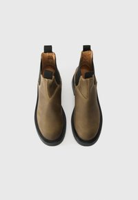 Καφέ δερμάτινα μποτάκια μέχρι τον αστράγαλο με μαύρες ελαστικές πλευρές, στρογγυλή μύτη και ανθεκτικές μαύρες καουτσούκ σόλες. Διαθέτουν θηλιά για εύκολη εφαρμογή.