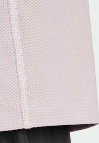 Ljusrosa texturerad sporttröja med maskformigt mönster och kontrastsömmar, med rak nederkant och lätt kurva vid kanterna.