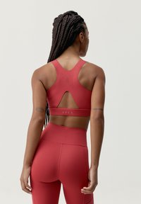 Röd idrotts-bh med racerback-design, med perforerade detaljer för andningsförmåga och en utskärning på baksidan.