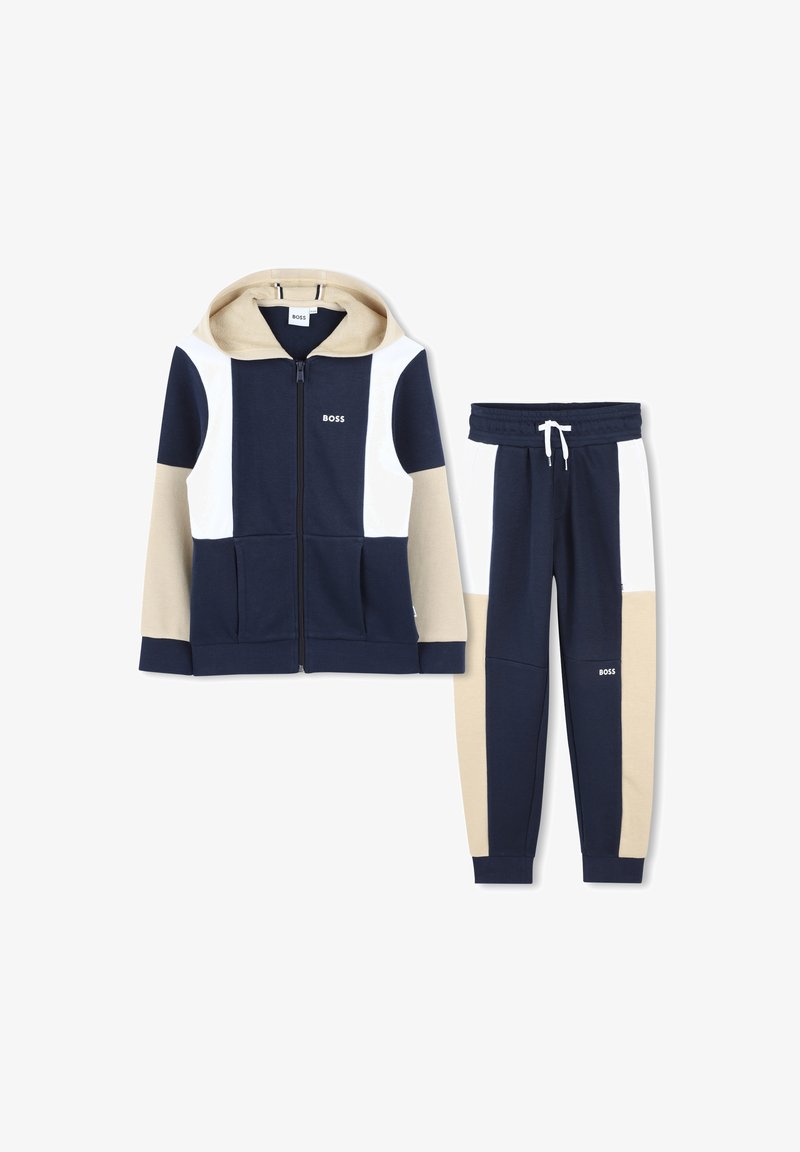 Marineblauwe en beige hoodie met witte accenten, rits aan de voorkant en zakken, gecombineerd met bijpassende broek met een elastische tailleband en logodetail.