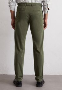 Zielone bawełniane spodnie o prostym kroju nogawki, wyposażone w dwie tylne kieszenie, zestawione z fakturowaną jasnoszaro koszulą i czarnymi butami.