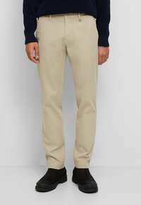 Beige chinos with a slim fit; smooth cotton fabric; discreet front pockets; worn with dark ankle boots; light-colored trousers.