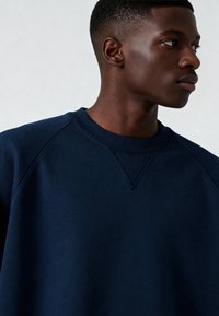 Felpa blu navy con scollo a coste e maniche raglan, realizzata in un tessuto liscio e morbido con cuciture minimali visibili.