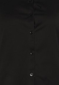 Svart skjorta med knappar fram, tillverkad av slätt tyg, med en rad svarta knappar på framsidan, en prydlig krage och inga synliga mönster.