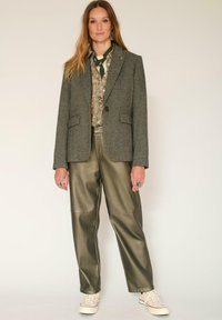 Blazer en tweed gris avec deux poches avant, associé à un pantalon en satin vert olive et des baskets beiges. Chemise à motif floral détaillé en dessous.