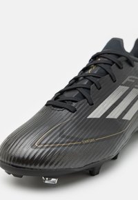 Ghete de fotbal negre cu un material superior texturat, dungi argintii și accente aurii. Prezintă un design aerodinamic și cleme transparente pentru tracțiune.