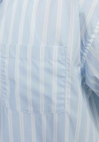 Camisa de color azul claro con finas rayas verticales blancas, que presenta un bolsillo en el pecho, tejido suave y mangas cortas.
