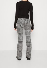 Czarna dopasowana bluzka z długim rękawem w połączeniu z szarymi i czarnymi spodniami w kratę houndstooth z rozkloszowanym krojem. Gładki materiał o delikatnej fakturze. Masywne czarne botki.