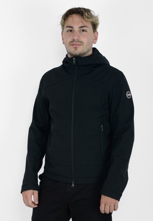 Giacca con cappuccio nera realizzata in materiale soft shell, dotata di una zip frontale, due tasche laterali e un logo sulla spalla sinistra.