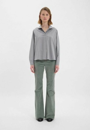 Chemise collée grise à rayures avec des manches oversized, associée à un pantalon évasé vert. Chaussures noires complètent la tenue. Fond uni.