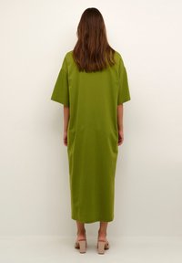 Grön bomullsoversized klänning med korta ärmar, som når till mitt på vaden, med avslappnad passform och enkel design, bärs tillsammans med beige blockklacksandaler.
