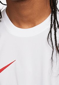 Person i en hvid skjorte med et rødt Nike swoosh-logo og flettet hår synligt på højre side.