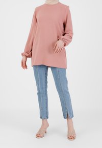 Różowa bluzka z długim rękawem i marszczonymi mankietami, w połączeniu ze jasnoniebieskimi prostymi dżinsami z bocznymi rozcięciami oraz jasnymi, plecionymi czółenkami na obcasie.