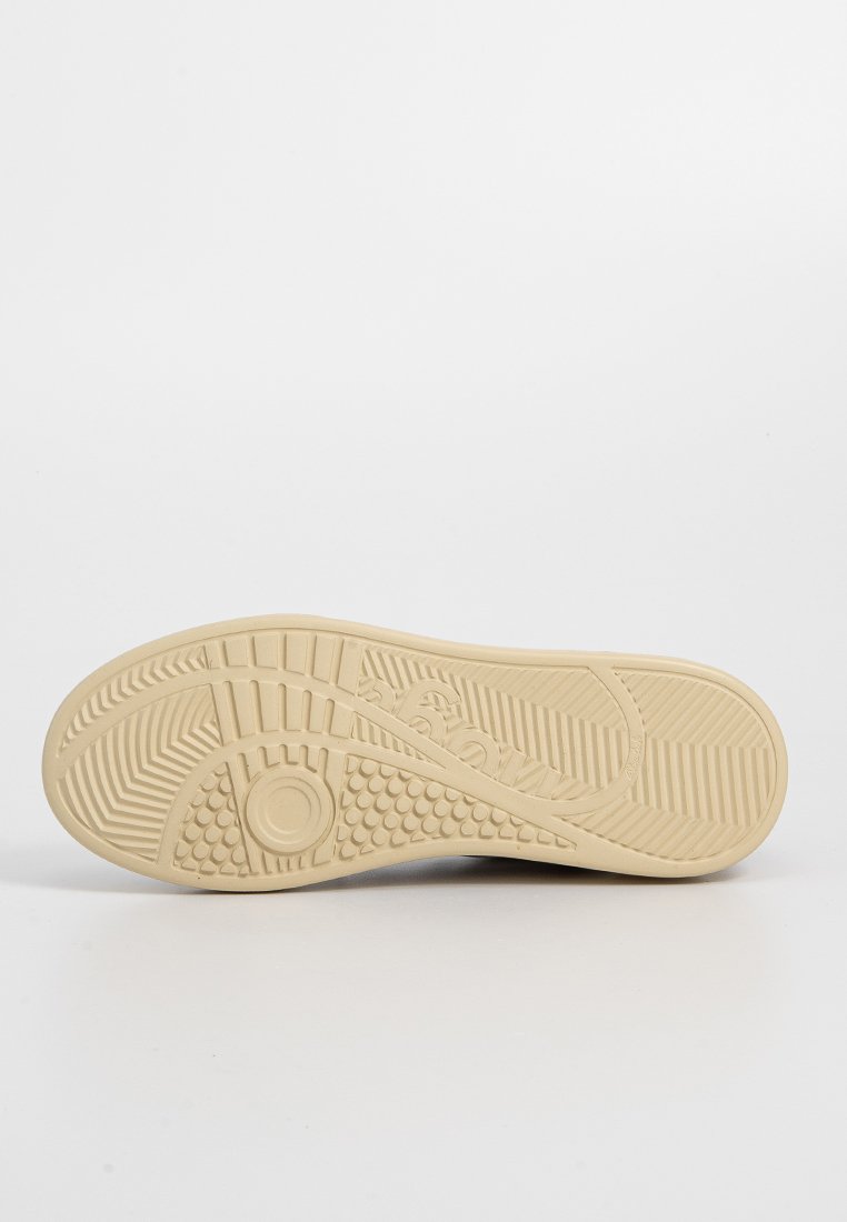 Suola di scarpa in gomma beige con modelli testurizzati, impugnature circolari e nervature per la trazione. Presenta un dettaglio del logo in rilievo vicino al tallone.