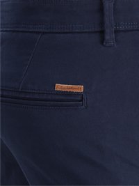 Pantalones de color azul marino hechos de algodón con una superficie texturada. Presentan un bolsillo trasero y una pequeña etiqueta de cuero marrón cerca de la cinturilla.