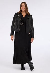 Jachetă moto din piele neagră peste o rochie maxi plisată neagră, cu curea. Bootcut negre, chunky, completează ținuta. Textură netedă, design mulat.
