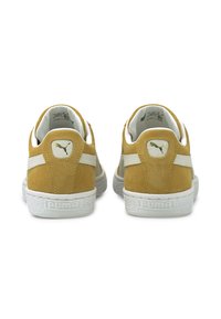 Żółte zamszowe trampki z białymi akcentami i gumową podeszwą, z logo na pięcie i teksturowaną powierzchnią. Klasyczny niski fason.