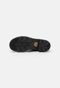 Black rubber shoe sole with star-shaped traction patterns and a brown accent label. Features grooves for enhanced grip and stability.