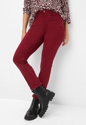 Burgunderfarbene Baumwoll-Stretch-Jeans mit schlankem Schnitt, umgeschlagenen Säumen und einem silbernen Knopf. Kombiniert mit schwarzen klobigen Stiefeletten.