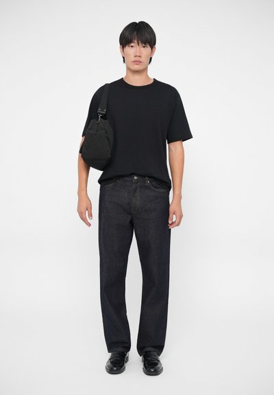 Camiseta negra de cuello redondo, jeans rectos de color azul oscuro, bolso cruzado negro y mocasines negros. Un atuendo casual y minimalista.